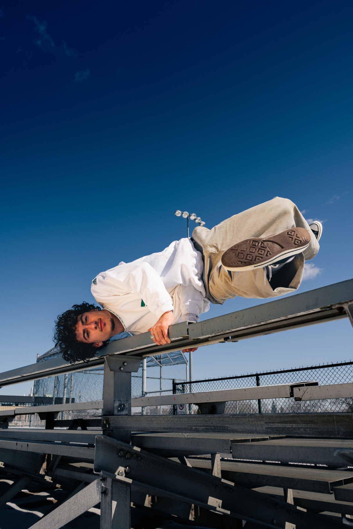 Dancer holding a freeze on metal bleachers under a deep blue sky.